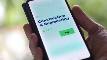 An investor's analyzing the construction & engineering etf fund on screen. A phone shows the ETF's prices stocks to invest