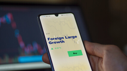 An investor's analyzing the foreign large growth etf fund on screen. A phone shows the ETF's prices trading growth to invest