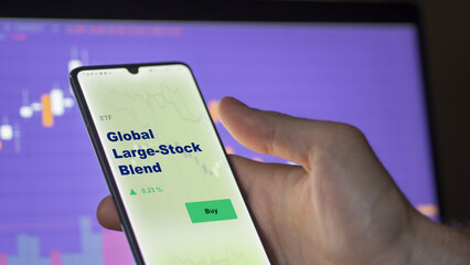 An investor's analyzing the global large stock blend stock blend etf fund on screen. A phone shows the ETF's prices stocks to invest