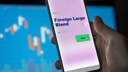 An investor's analyzing the foreign large blend etf fund on screen. A phone shows the ETF's prices stocks to invest