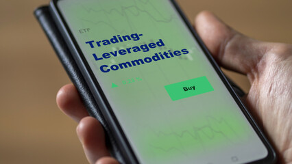 An investor's analyzing the trading leveraged commodities etf fund on screen. A phone shows the ETF's prices stocks to invest