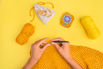 Top view of woman's hands with crochet hook and unfinished piece of crochet net with balls of yarn and decorative elements near - obrazy, fototapety, plakaty