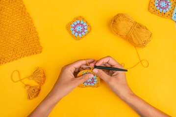 Top view of hands crocheting square element on yellow background with different crocht patterns,...