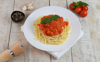 Spaghetti or pasta with tomato sauce and fresh green basil on a white plate with cherry tomato on wooden table