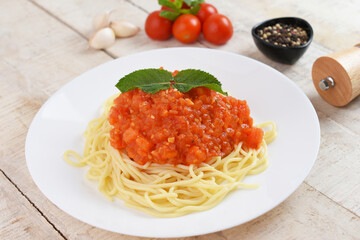 Spaghetti or pasta with tomato sauce and fresh green basil on a white plate with cherry tomato on wooden table.