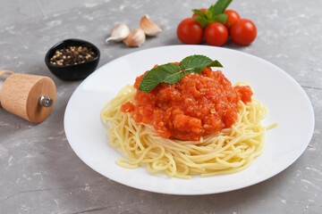 Spaghetti or pasta with tomato sauce and fresh green basil on a white plate with cherry tomato on wooden table.