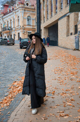 romantic beautiful brunette smiling girl in a black hat walking in the autumn city