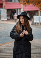 romantic beautiful brunette smiling girl in a black hat walking in the autumn city