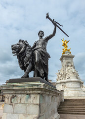 Fototapeta na wymiar London, England, UK - July 6, 2022: Victoria Memorial. Closeup of Black bronze Progress statue of lion, youth with flaming torch under blue cloudscape. Central marble monument in back