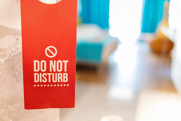 ''Do not disturb'' sign on a handle of hotel room door with bed in the background. Hotel door handle with a do not disturb sign request.