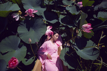 portrait beautiful brunette woman in a pink dress is lies on a boat among blooming lotuses on a...