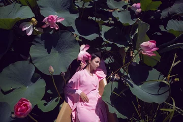 Poster portrait beautiful brunette woman in a pink dress is lies on a boat among blooming lotuses on a lake in Astrakhan. © saulich84