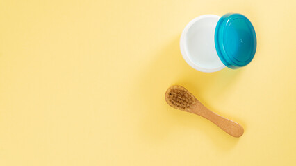Cream jar and massage brush on a yellow background with text space