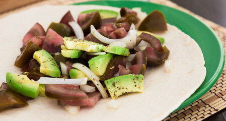 salad of black tomatoes, avocado and onions in Italian tortilla on green plate
