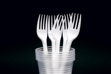 Disposable plastic forks and glasses on a black background. Disposable utensils for eating and drinking at a picnic or outdoors. Convenient disposable food and drink accessory