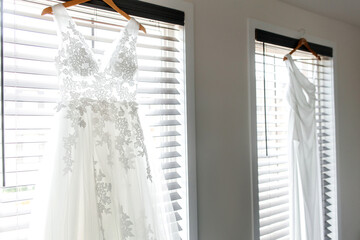 Bedroom with two women's wedding dresses for a lesbian LGBT wedding. Side view of beautiful white wedding dresses in a room against the background of windows for a same-sex wedding of two brides