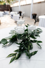 Tables for guests are decorated with floating candles and green leaves. Preparing for an outdoor party with candles and leaf decor. Decor in the form of candles close-up on the table with leaves