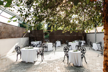 A beautiful restaurant with a transparent roof and decorated tables and live trees. Party preparation and table setting. Beautiful location with black tables and white tablecloths for receiving guests