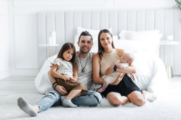 Portrait of happy young parents and their little children in the bedroom. Dad mom their little daughter and newborn son. Happy young family having fun with each other posing for photographer
