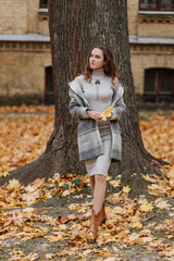  Young smiling girl in a gray coat holds a yellow leaf in her hands