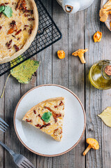 Homemade quiche or tart with chanterelles on rustic wooden background.