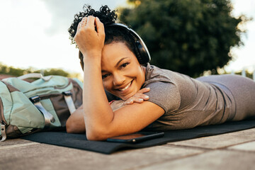 Photo of cheerful sportswoman smiling and lying on fitness mat while working out in urban park