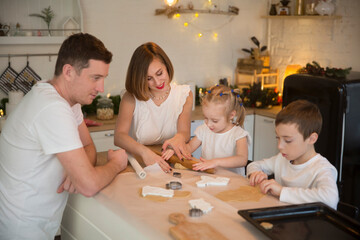 happy family dad, mom and two kids make Christmas cookies and have fun together at home in the kitchen.  Children siblings making homemade xmas gingerbreads