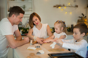 happy family dad, mom and two kids make Christmas cookies and have fun together at home in the kitchen.  Children siblings making homemade xmas gingerbreads