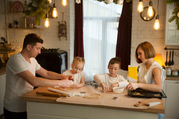 happy family dad, mom and two kids make Christmas cookies and have fun together at home in the kitchen.  Children siblings making homemade xmas gingerbreads