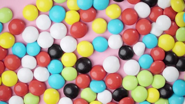 Multi-colored candy dragees move shaking against a pink background in motion