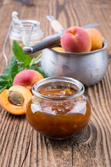 Traditional German apricot jam with fresh fruits offered as close-up canning jar glass on a wooden board