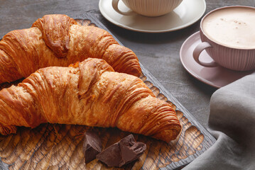 Kitchen wooden board with tasty croissants and chocolate and cup of coffee on dark table, close up. French pastry. Selective focus