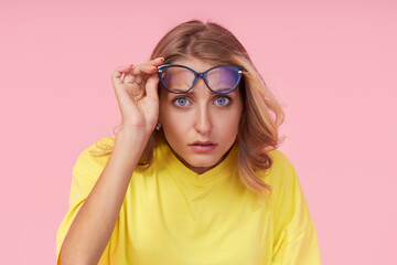 Portrait of young excited woman in glasses, yellow casual t-shirt on pink background. Surprised and incredulous looks wide open mouth and eyes