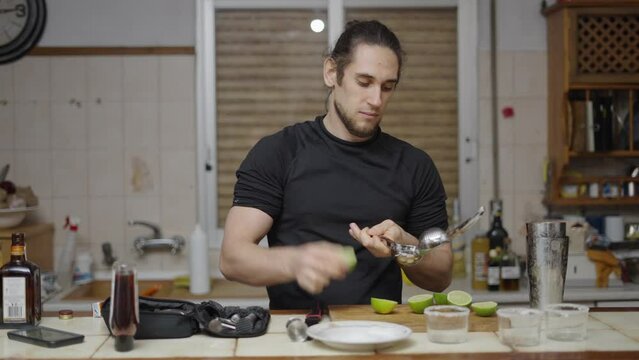 Young attractive barman using lemon squeezer to obtain juice for cocktail. Puts juice in cocktail shaker. 