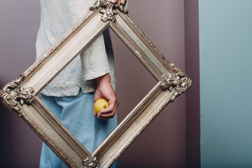 Millenial young man holds apple on hand palm in gilded picture frame