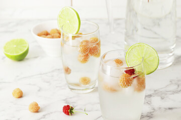 Glass and jug with fresh water and lime on marble table. Space for text. Flavored water. Summer drinks. Raspberry, mint and lime.
