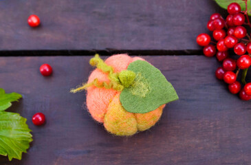 Pumpkin made using the technique of dry felting on wooden boards surrounded by viburnum berries