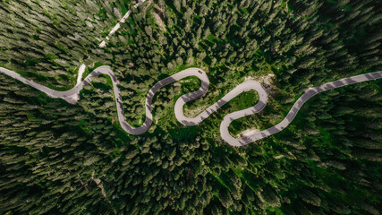 Winding road from high mountain pass in Dolomites, Italy. Great road trip through dense woods and meadows. Aerial view. Curvy road in summer forest scenery, mountain landscape.Top Down Birds Eye View.