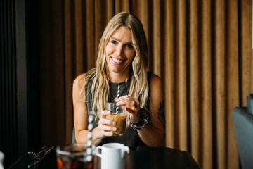 Woman holding iced coffee with a paper straw at table, looking at camera and smiling