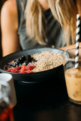 Shallow focus on a bowl of oatmeal, yogurt and fruit with an iced coffee in foreground, person in background