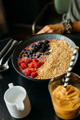 Shallow focus on a bowl of oatmeal, yogurt and fruit with an iced coffee in foreground, person in background