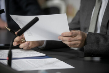 One of politician sitting by table with his hands over document during political summit or conference