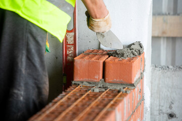 Bricklayer worker installing brick masonry on exterior wall with trowel putty knife