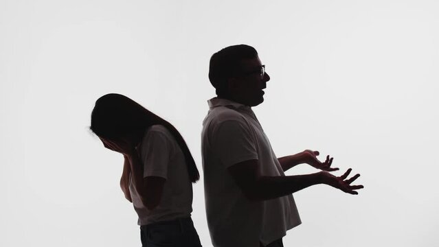 Unrecognizable couple arguing standing back to back against the white background. Angry man gestures with his hands. Woman holds her face, sobbing, crying. Marriage problems, toxic relationship