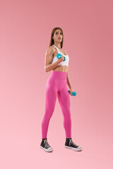 Fototapeta na wymiar A young female trainer in pink and white sportswear poses with two dumbbells in her hands isolated on a pastel light pink background. Training sport concept.