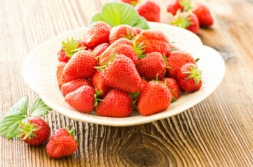 Ripe red strawberries from organic cultivation offered as close-up in a rustic design bowl on a brown wooden board