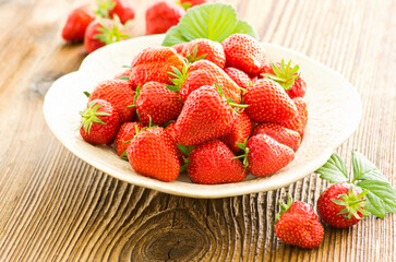 Ripe red strawberries from organic cultivation offered as close-up in a rustic design bowl on a brown wooden board