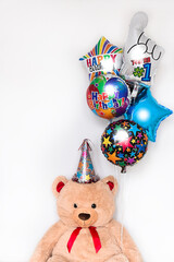 Large teddy bear in birthday hat with party balloons isolated on white background