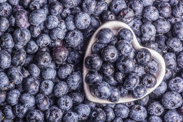 Juicy blueberries in a bowl on a berry background.