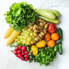 Buying natural fruits, vegetables and greens concept. Salad leaves, cabbages, corn, grapes, lemons, tomatoes, parsley lying on the kitchen table, top view. Square composition.